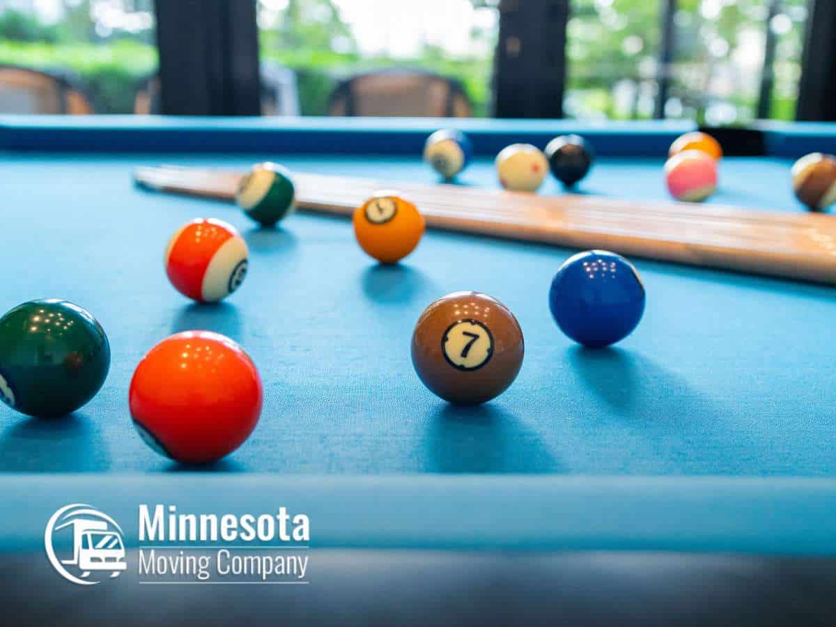 Pool balls scattered on a table with cues in the background, promoting services to move a pool table by Minnesota Moving Company.
